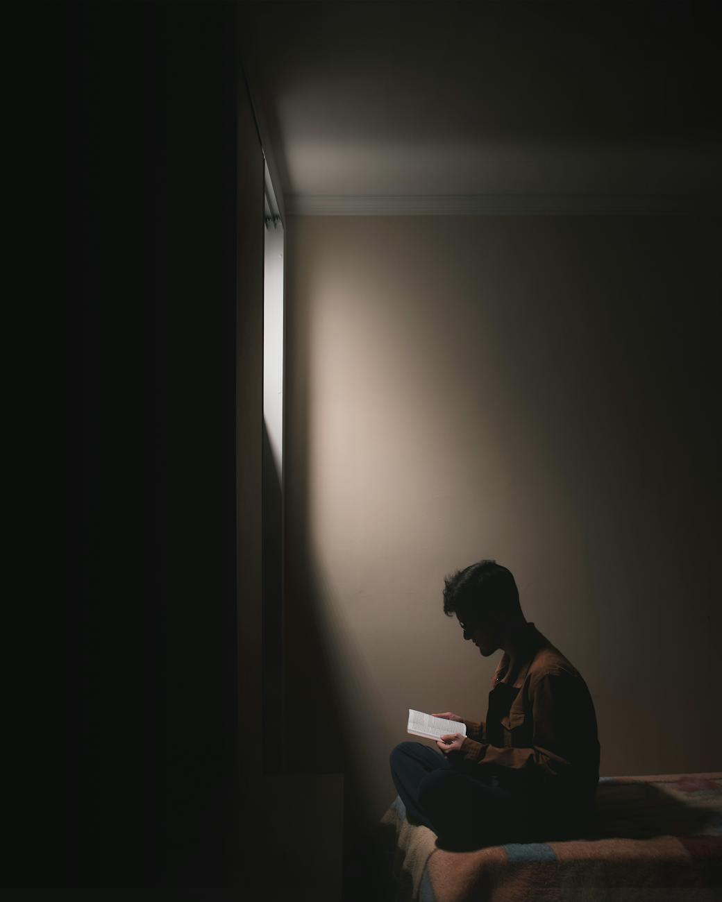 a man reading book while sitting on a bed